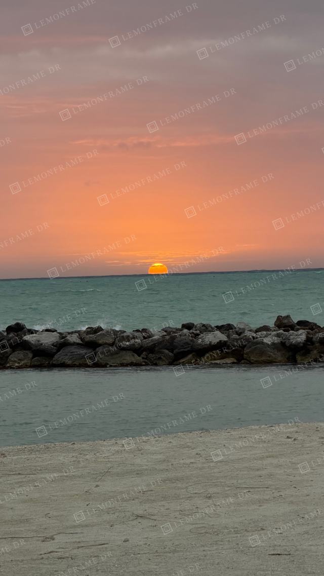 Sol rosado sobre el agua turquesa y el rompeolas
